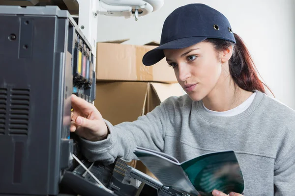 Senhora com livro de instruções trabalhando na fotocopiadora — Fotografia de Stock
