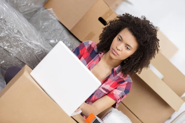 Beautiful woman using a laptop while unpacking box at home — Stock Photo, Image