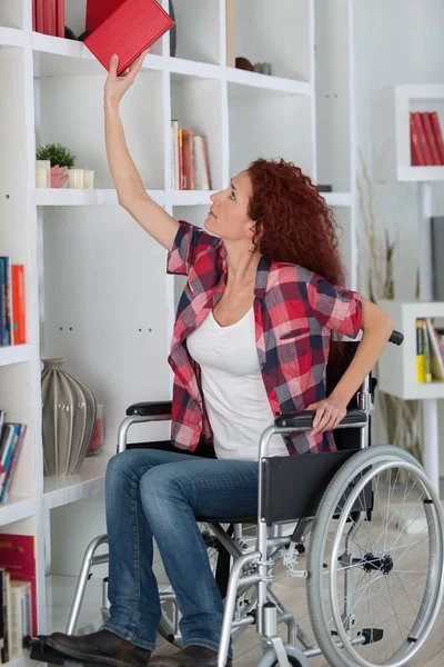 Mujer discapacitada luchando para llegar a un libro en el estante superior —  Fotos de Stock