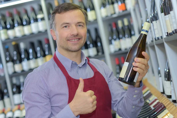 Retalhista segurando garrafa de vinho e fazendo gesto positivo — Fotografia de Stock