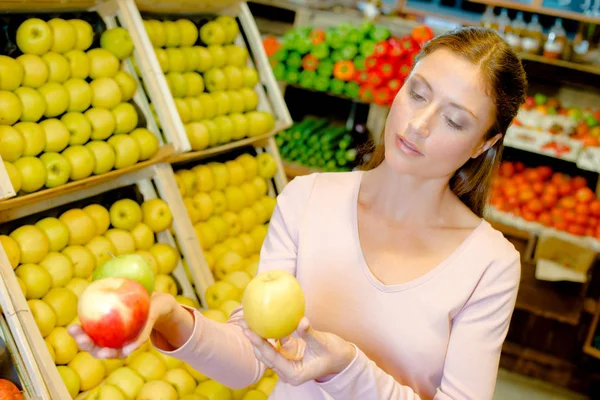 Ung kvinna överväger äpplen — Stockfoto