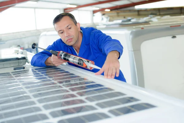 El hombre sellando alrededor del panel solar en el techo del vehículo — Foto de Stock