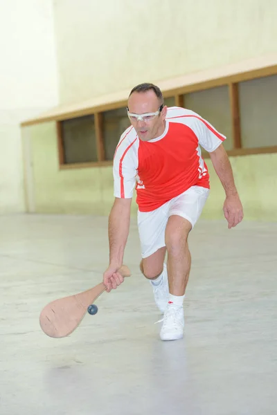 Sportman bereiken voor bal met houten racket — Stockfoto