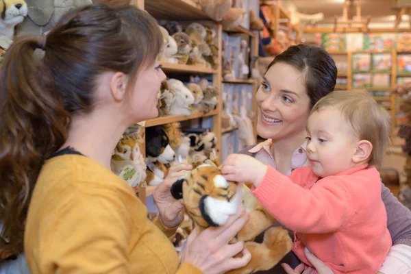 Madre e hija con vendedor atractivo en tienda de juguetes —  Fotos de Stock