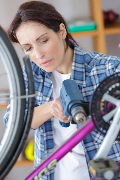 Mujer joven está arreglando su bicicleta —  Fotos de Stock