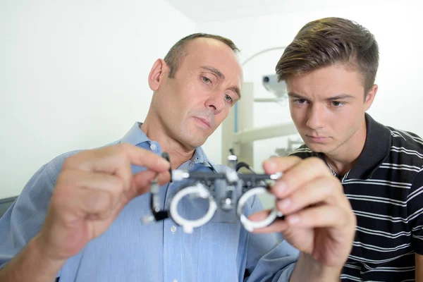 Optician mostrando óculos de teste para o jovem — Fotografia de Stock