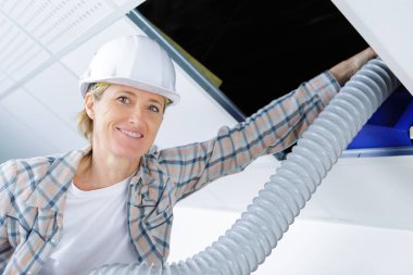 female worker fitting ventilation system in buildings ceiling clipart