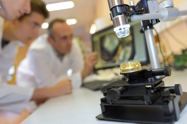 Close up of microscope, students in background — стоковое фото