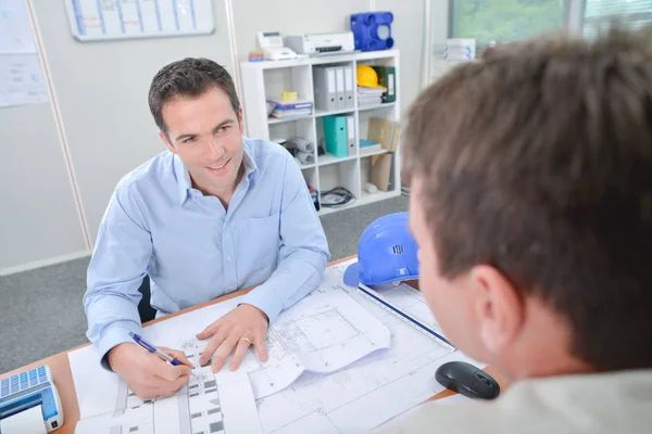 Två män vid skrivbord diskuterar ritningar — Stockfoto