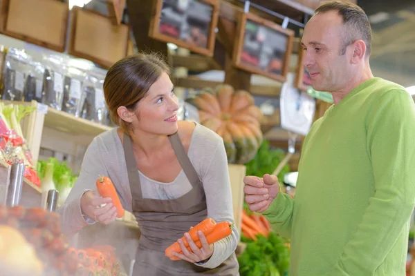 Assistente de vendas com cliente, segurando cenouras — Fotografia de Stock