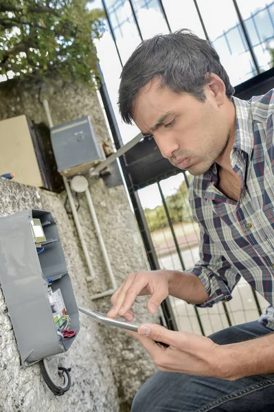 Homem trabalhando na caixa na parede exterior, segurando tablet — Fotografia de Stock