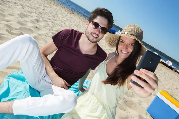 Lindo jovem casal sentado na praia e fazendo selfie — Fotografia de Stock