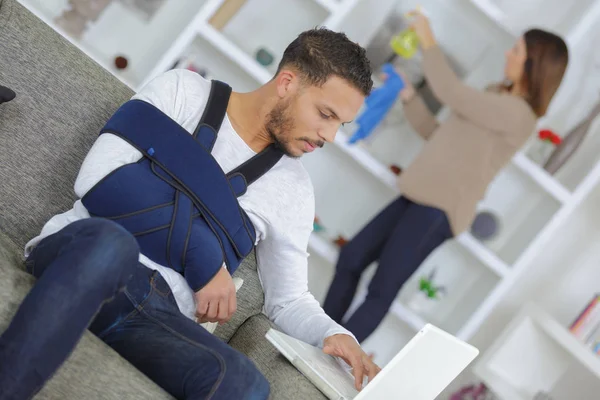 Man with arm in sling using laptop computer — Stock Photo, Image