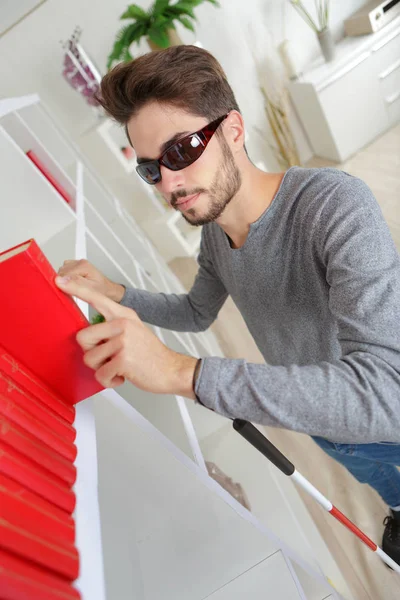 Blind man reading braille on spine of book — Stock Photo, Image