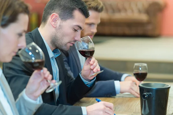 Tres personas oliendo y evaluando el vino tinto en las gafas de vino —  Fotos de Stock
