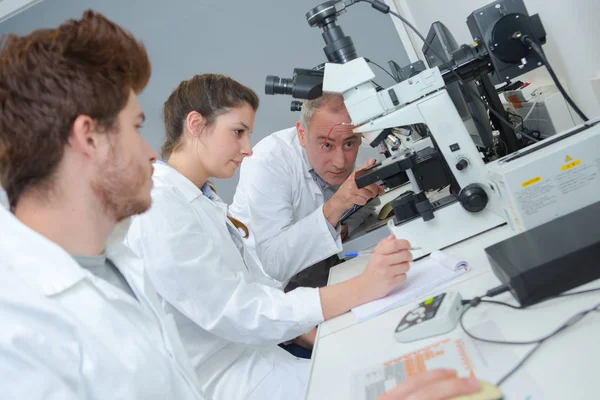 Profesor instruyendo a los estudiantes sobre el uso del microscopio — Foto de Stock