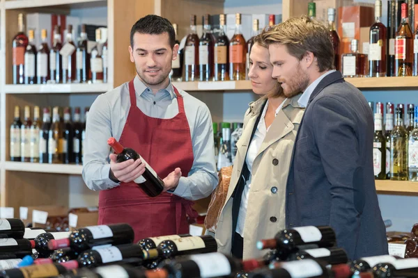 Wind merchant recommending a bottle to young couple — Stock Photo, Image