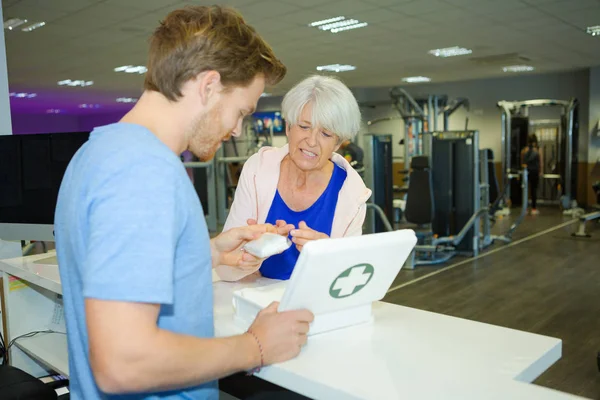 Hombre en el gimnasio dando yeso a la señora con el dedo cortado — Foto de Stock