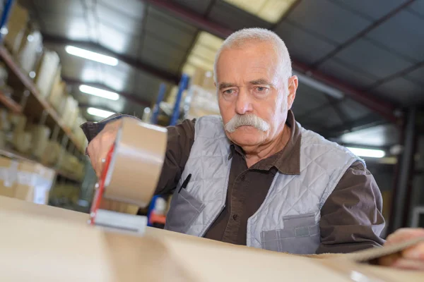 Senior homme étanchéité boîte en carton avec un distributeur de ruban adhésif — Photo