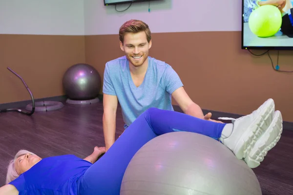 Fisioterapeuta guiando las piernas de los pacientes en la bola aeróbica — Foto de Stock