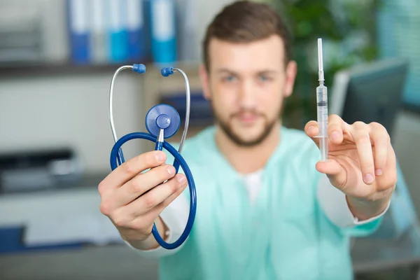 Médico masculino segurando para a frente um estetoscópio e uma seringa — Fotografia de Stock