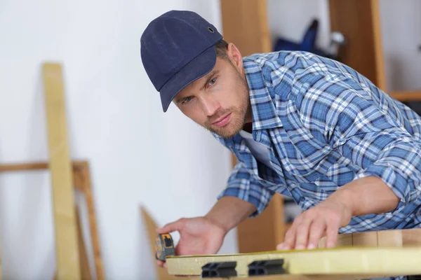 Picture of young man working as carpenter and measuring board — Stock Photo, Image