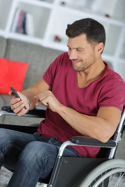 Schöner Mann im Rollstuhl, der auf seinem Handy SMS schreibt — Stockfoto