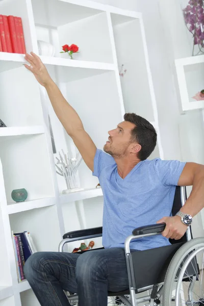 Handikappade mannen välja en bok från bokhyllan — Stockfoto