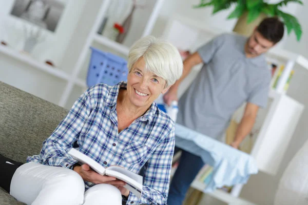 Damen som läser en bok medan mannen strykjärn i bakgrunden — Stockfoto