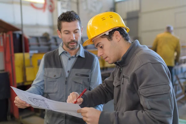 Ouvrier en uniforme montrant à son patron le plan de l'usine — Photo