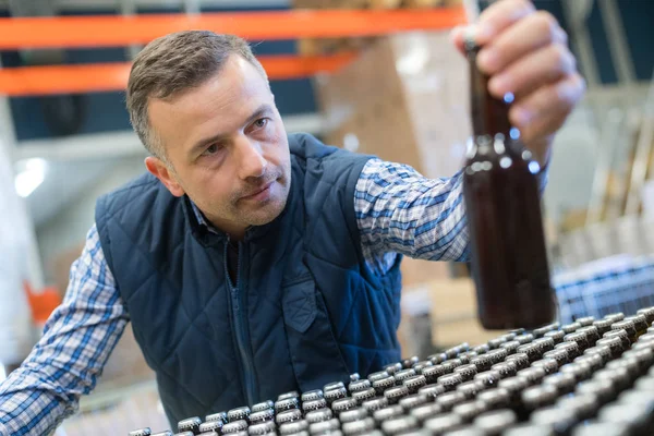 Homem inspecionando garrafa feita de vidro marrom — Fotografia de Stock