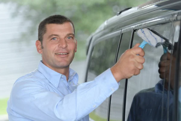 Мужчина моет окна машины с помощью скребка — стоковое фото