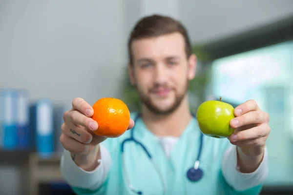 Doctor sosteniendo una manzana y naranja en sus manos — Foto de Stock