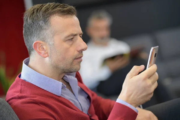 Mann im Wartezimmer blickt auf sein Telefon — Stockfoto