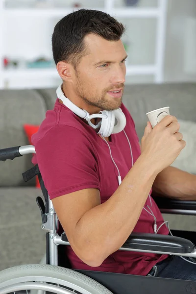 Hombre guapo escuchando música en los auriculares mientras está sentado en silla de ruedas — Foto de Stock