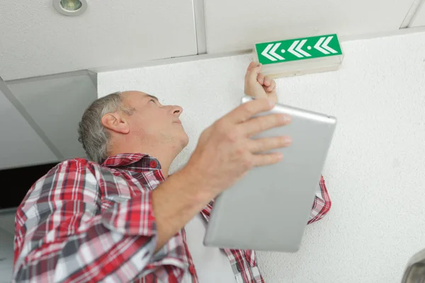 Uomo in possesso di tablet, controllo segnale di uscita di emergenza — Foto Stock