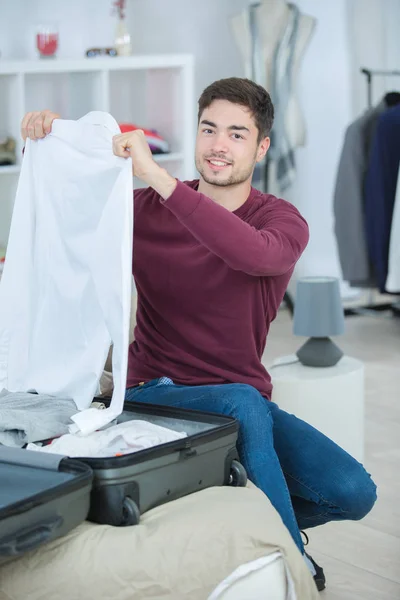 Мужчина держит чистую рубашку, чтобы упаковать ее в чемодан — стоковое фото