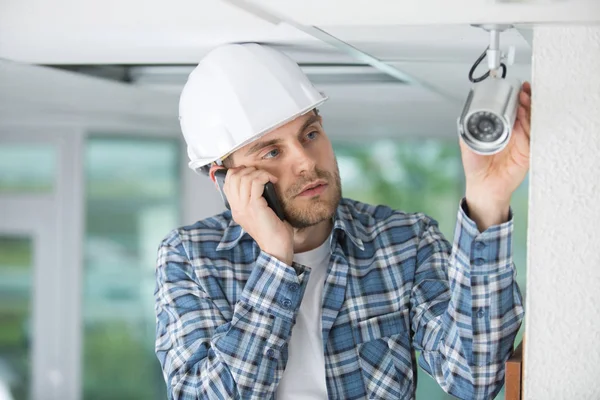 Junger Bauunternehmer telefoniert beim Anblick von Indoor-Überwachungskamera — Stockfoto