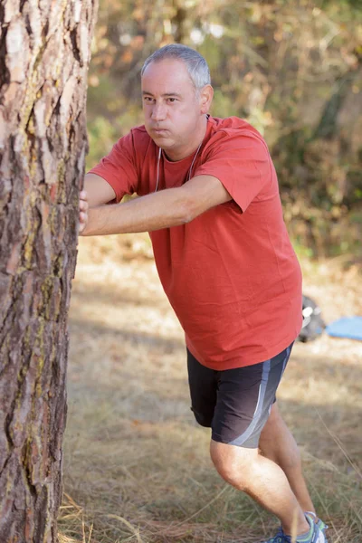 Hombre apoyado en el árbol para estirar —  Fotos de Stock