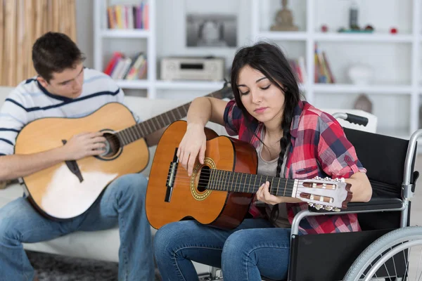 Дві молоді люди грають на гітарі, одна в інвалідному візку — стокове фото