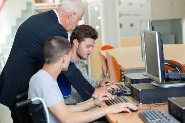 Enseignant aidant les jeunes hommes à utiliser des ordinateurs, un en fauteuil roulant — Photo