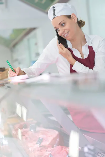 Donna al bancone della carne prendere ordine telefonico — Foto Stock