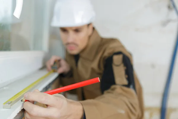 Bauarbeiter misst ein Fenster mit Maßband und Bleistift — Stockfoto