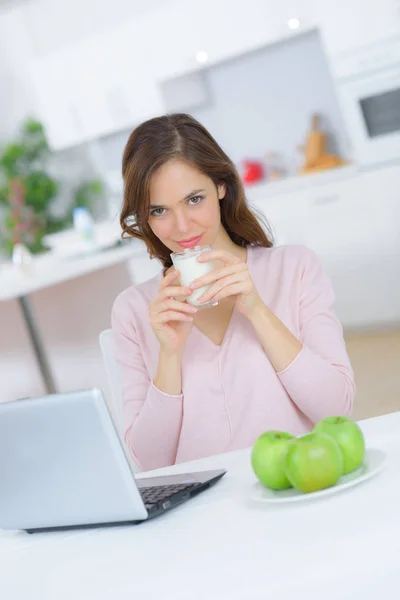 Mulher usando laptop em casa, bebendo um copo de leite — Fotografia de Stock