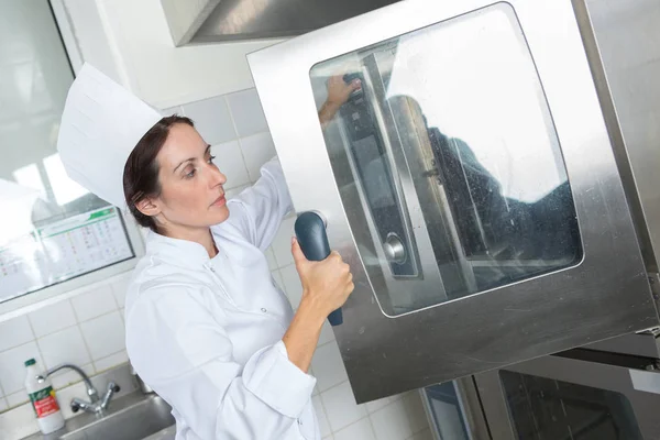 Female chef opening oven door — Stock Photo, Image