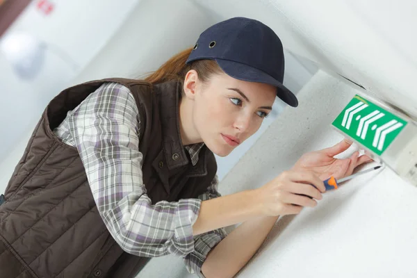 Señorita joven instalando señal de salida de emergencia a la pared —  Fotos de Stock