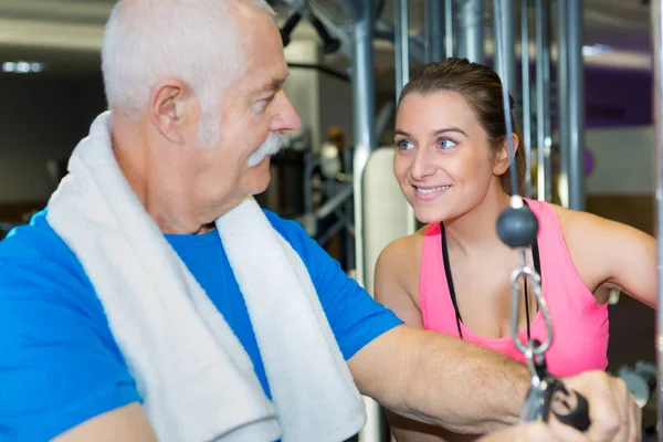 Äldre man och hans tränare leende i fitnesstudion — Stockfoto