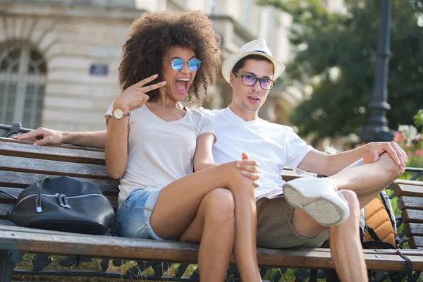 Young couple sat on bench, woman making funky gesture — Stock Photo, Image