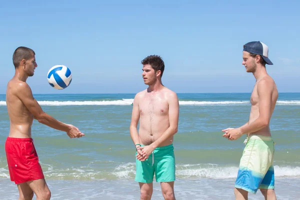 Unga män leker med boll på stranden — Stockfoto