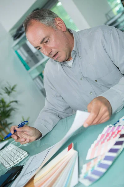 Seniorchef am Schreibtisch, umgeben von Farbkarten — Stockfoto